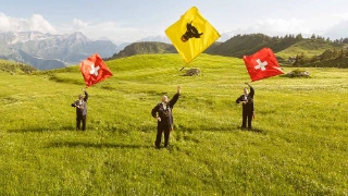 Drei traditionelle Männer aus Uri auf einer Wiese am Fahnenschwingen, im Hintergrund die Urne Bergkulisse.